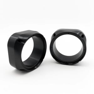 May include: Two black, ring-shaped metal components with rounded edges. Each component has a large central opening and several small holes. The objects are set against a white background, highlighting their shape and design.