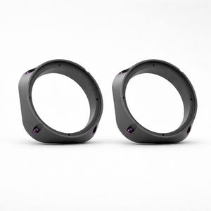 May include: Two dark gray, circular objects with a rounded rectangular shape. Each has a large central opening and several small, purple-colored fasteners. The objects are set against a white background.