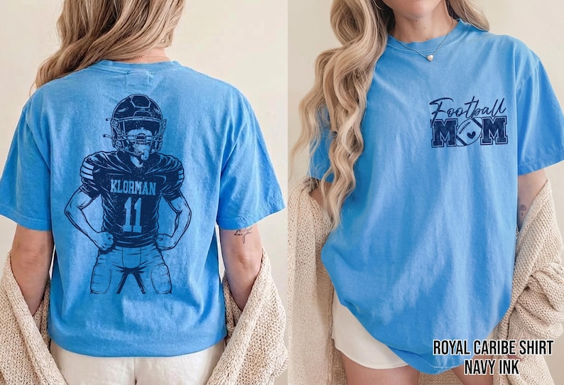 May include: A light blue t-shirt featuring a dark blue graphic on the back of a football player wearing a helmet and jersey with the name KLORMAN and number 11. The front chest area displays the text Football MOM with a football graphic.