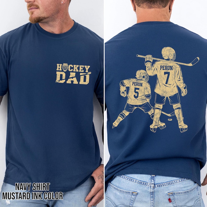 May include: Navy blue t-shirt with "HOCKEY DAD" in mustard yellow on the front. The back features a hockey player graphic with the name "PERUN" and the number "7" and "5". The shirt's color is navy with mustard yellow ink.