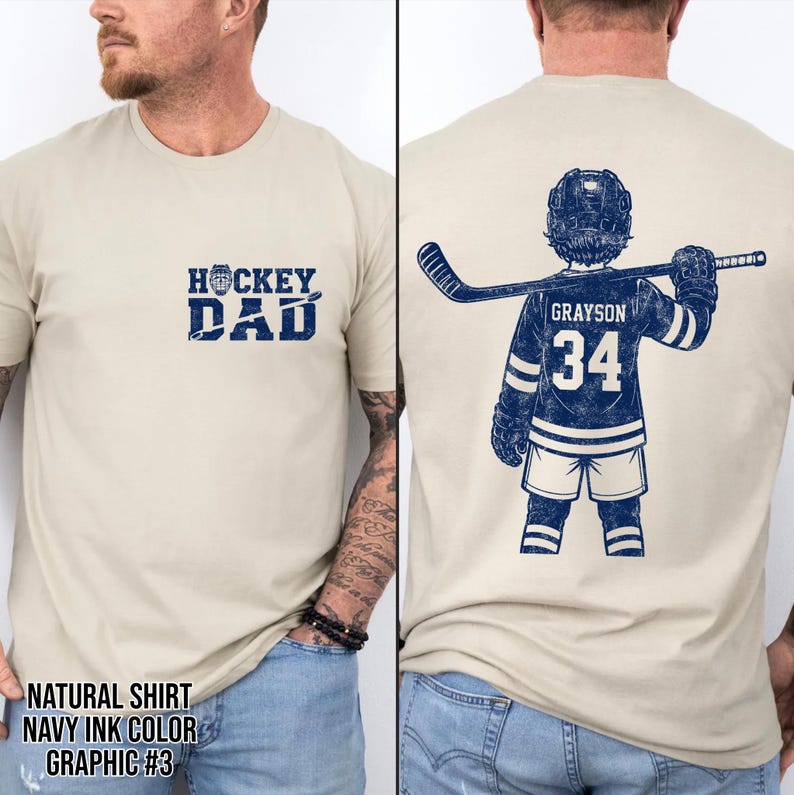 Pode incluir: Uma camiseta de cor natural com tinta azul marinho. A frente apresenta o texto "HOCKEY DAD" acima de um gr&aacute;fico de disco e taco de h&oacute;quei. A parte de tr&aacute;s mostra um gr&aacute;fico de jogador de h&oacute;quei com o nome "GRAYSON" e o n&uacute;mero "34".