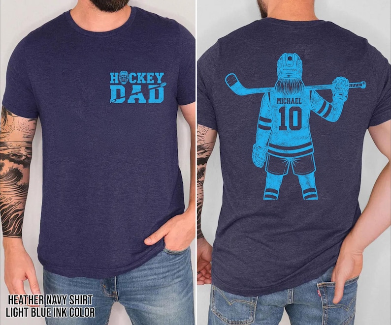 Pode incluir: T-shirt azul marinho mesclado com tinta azul clara. A frente da camisa tem o texto "HOCKEY DAD". A parte de tr&aacute;s da camisa apresenta um gr&aacute;fico de jogador de h&oacute;quei com o nome "MICHAEL" e o n&uacute;mero "10".