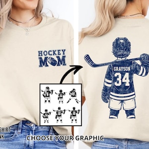 May include: A cream-coloured t-shirt with a navy blue "Hockey Mom" graphic on the front. The back features a navy blue hockey player jersey with the name "Grayson" and the number "34". Includes a graphic selection.