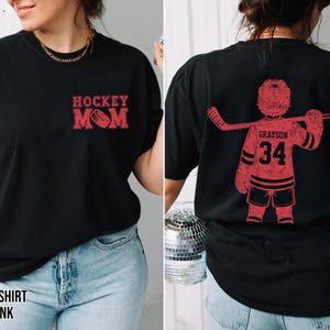 May include: Black t-shirt with red ink. The front features "Hockey Mom" with a hockey puck graphic. The back displays a red hockey player graphic with the name "Grayson" and the number "34".