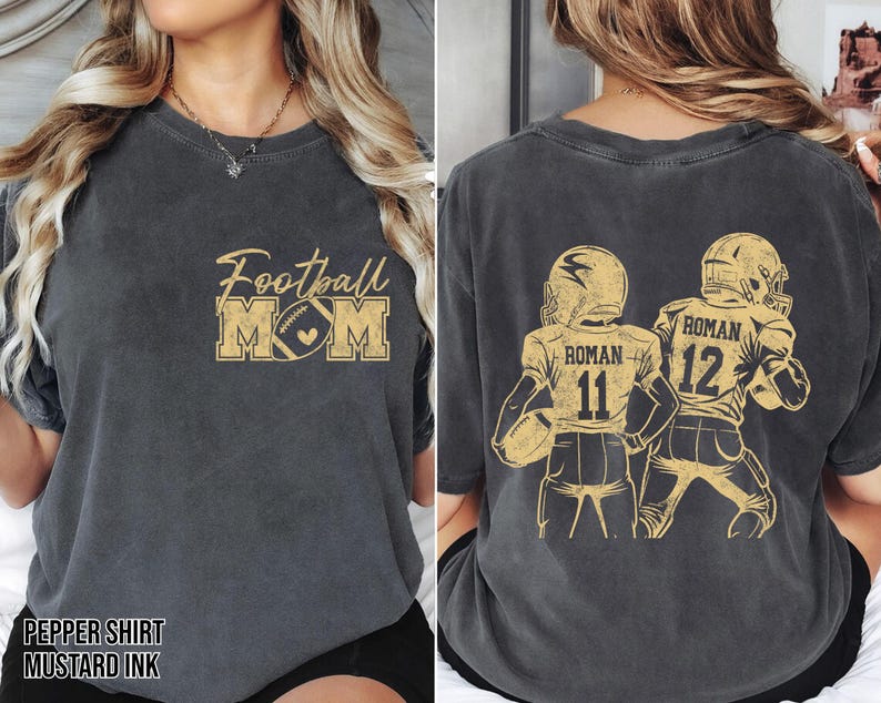 May include: A charcoal gray short-sleeve t-shirt with mustard yellow graphics. The front features the text Football MOM with a football icon. The back displays two football players in jerseys with the name ROMAN and numbers 11 and 12.