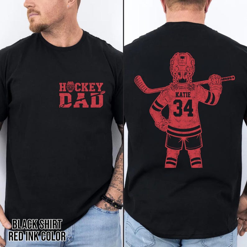 May include: Black t-shirt with red ink design. The front features the text "HOCKEY DAD". The back displays a hockey player graphic with the name "KATIE" and the number "34". The shirt is a classic crew neck style.