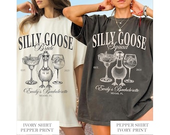 May include: Ivory and pepper-colored t-shirts with a graphic design featuring a goose wearing a veil and sunglasses, and two cocktail glasses. The text reads "Silly Goose Bride" and "Silly Goose Squad" with "Emily's Bachelorette, Miami, FL" below.