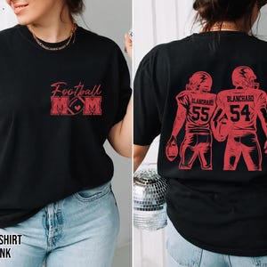 May include: A black t-shirt featuring red ink graphics. The front displays the text Football MOM with a football icon. The back shows two football players in helmets and jerseys with the name BLANCHARD and the numbers 55 and 54 in red ink.