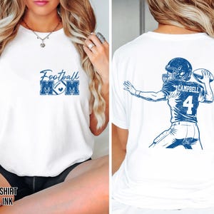 May include: A white t-shirt with royal blue ink graphics. The front features the text Football MOM with a football icon. The back displays a detailed illustration of a football player in a jersey with the name CAMPBELL and the number 4.