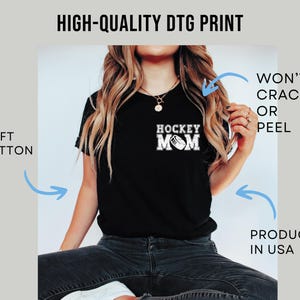 May include: Black t-shirt with the text "HOCKEY MOM" in white, featuring a hockey puck graphic. The image also includes the text "HIGH-QUALITY DTG PRINT", "SOFT COTTON", "WON'T CRACK OR PEEL", and "PRODUCED IN USA".