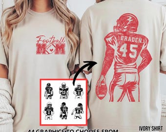 May include: An ivory t-shirt featuring red ink graphics. The front displays the text Football MOM with a football icon. The back shows a football player graphic with the name BRADEN and number 45. A small inset shows six player options.