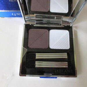 May include: A silver compact eyeshadow palette with two shades: a dark purple and a light white. The palette includes two applicators and the text "ORLANE PARIS" on the bottom.
