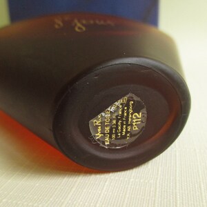 May include: A brown perfume bottle with a rounded shape. The bottle has a label with text including "EAU DE TOILETTE" and "100 ml 3.38 FL. OZ.". The bottle is made in France.
