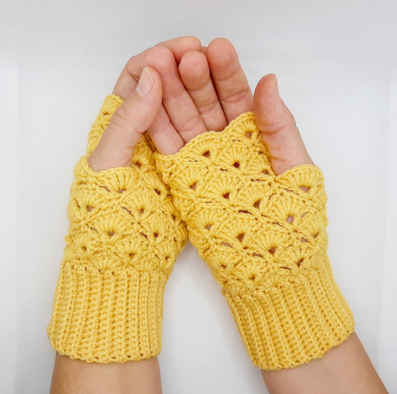 May include: A pair of yellow crocheted fingerless gloves with a lacy pattern. The gloves are made with a soft yarn and have a comfortable fit.