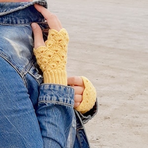 May include: A pair of yellow crocheted fingerless gloves. The gloves have a lacy pattern and are made with a soft yarn.