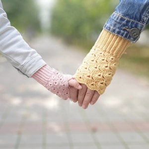 May include: Two people holding hands, wearing crocheted fingerless gloves. The gloves are pink and yellow with a lacy pattern.