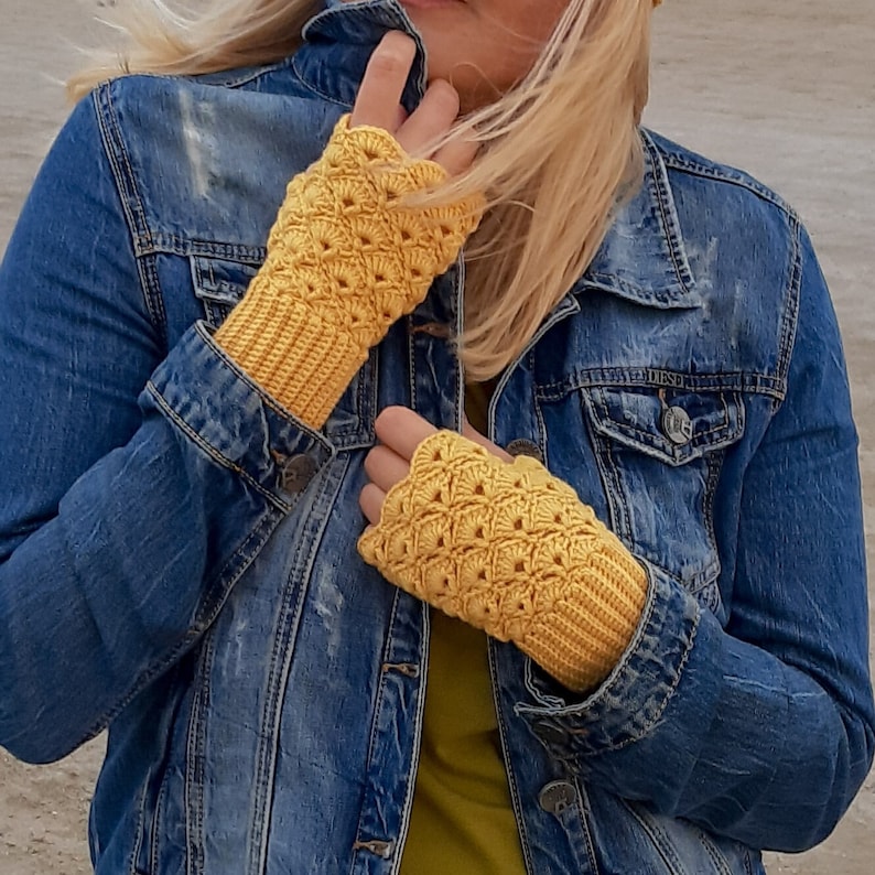 May include: A pair of yellow crocheted fingerless gloves with a textured pattern. The gloves are worn by a person wearing a denim jacket.
