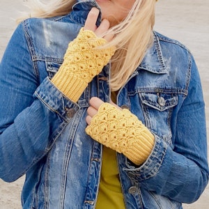 May include: A person wearing a denim jacket with yellow crocheted fingerless gloves. The gloves have a lacy pattern.