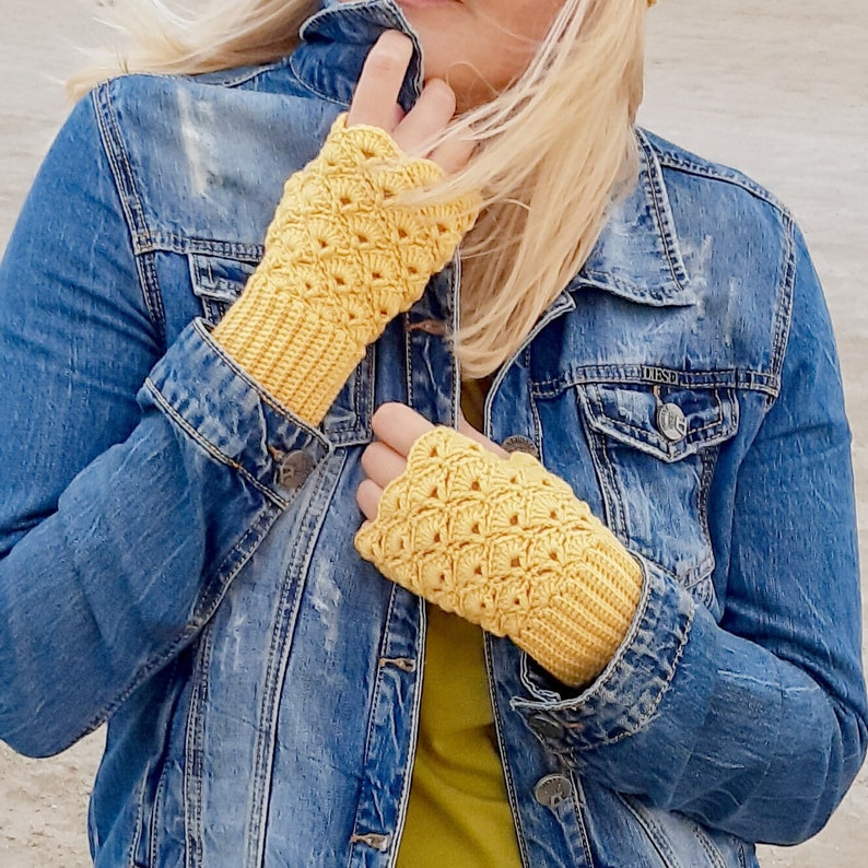 May include: A person wearing a denim jacket with yellow crocheted fingerless gloves. The gloves have a lacy pattern.