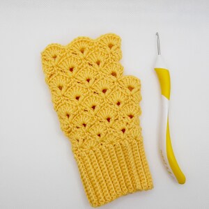 May include: A yellow crocheted fingerless glove with a scalloped edge and a crochet hook.