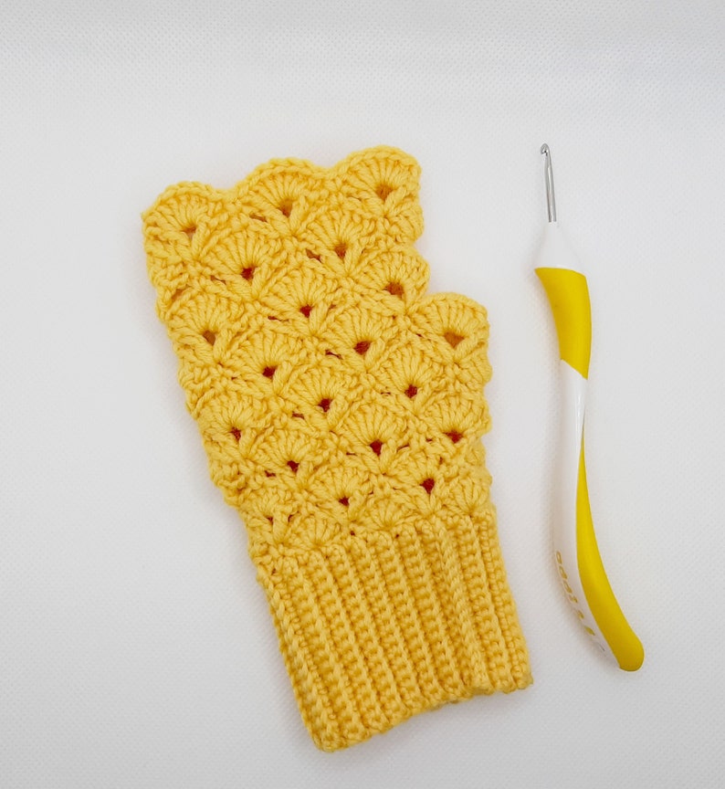 May include: A yellow crocheted fingerless glove with a scalloped edge and a crochet hook.