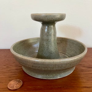 May include: A green ceramic ring holder with a raised center section. The holder has a speckled finish.