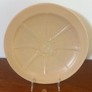 Puede incluir: Un plato grande de cerámica de color beige con un diseño de rueda. El plato tiene un centro elevado con un patrón circular.