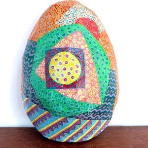 May include: A colorful, decorative egg with a patchwork design. The egg features a variety of patterns and colors, including orange, green, pink, and blue. The egg is approximately 6 inches tall.