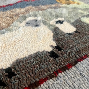 May include: Close-up of a hand-stitched rug featuring two sheep, one white and one black, with a brown and red border.