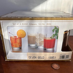 May include: A box of Devon Gold glasses, a set of 4, 14 ounce glasses. The box is white with gold trim and features a picture of the glasses filled with different beverages. The text on the box reads "Set of 4 D.O.F. Glasses, 14 Oz. (024)" and "DEVON GOLD (685)".