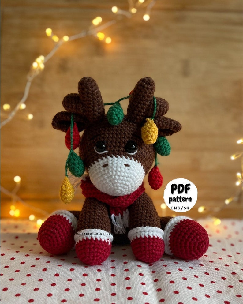 Crochet Reindeer, dark brown in color with white muzzle, he is wearing red and white Christmas shoes on all 4 legs, he has red and white scarfs around his neck and colorful Christmassy lights hanging on his antlers. He is 13sc tall then sitting.