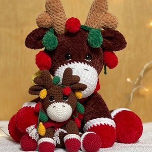 May include: Two crocheted reindeer ornaments, one large and one small, with red, green, and yellow lights. The reindeer are sitting on a white surface.