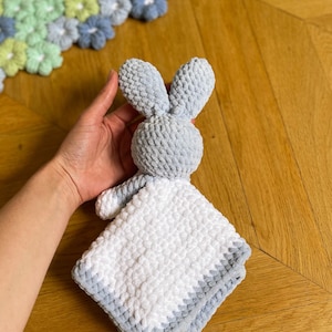 Puede incluir: Una manta de beb&eacute; suave y mullida en forma de conejo, de color gris y blanco, con textura de ganchillo.