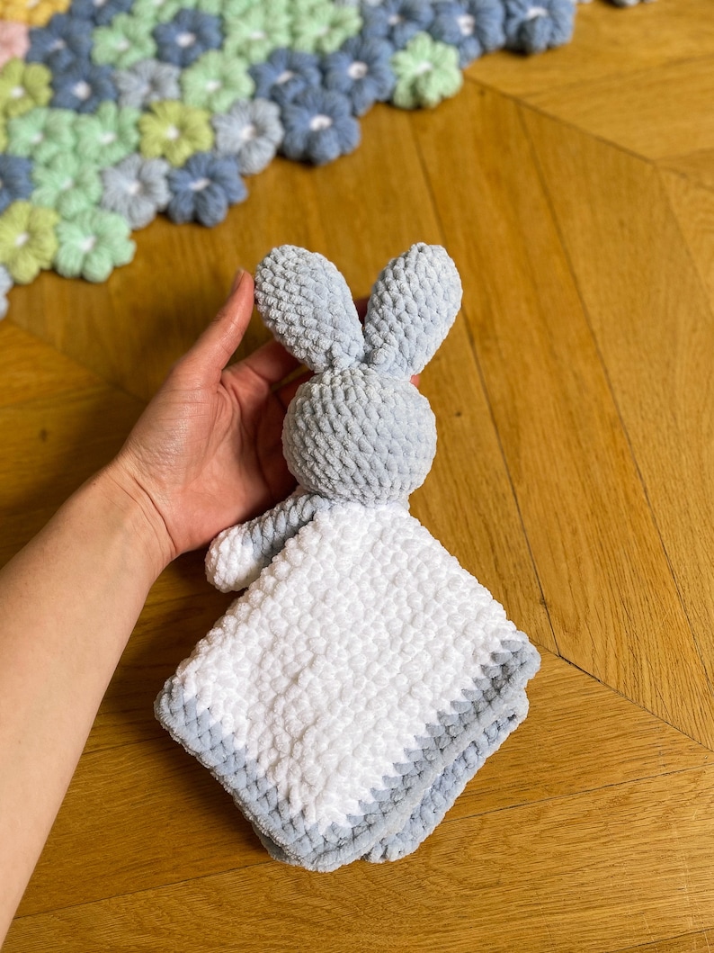 Puede incluir: Una manta de beb&eacute; suave y mullida en forma de conejo, de color gris y blanco, con textura de ganchillo.
