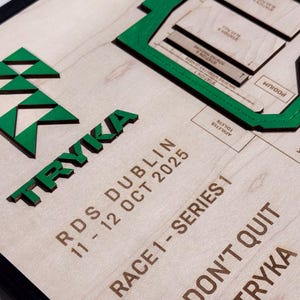 May include: Wooden plaque with the word "TRYKA" in green, along with event details: "RDS DUBLIN 11-12 OCT 2025" and "RACE1-SERIES 1". A green geometric design and a map-like graphic are also present.