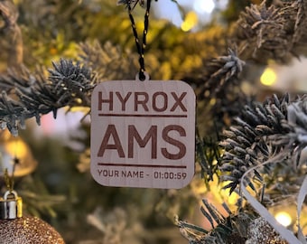 May include: A wooden Christmas bauble with the text "HYROX AMS" and "YOUR NAME - 01:00:59" hanging on a Christmas tree.