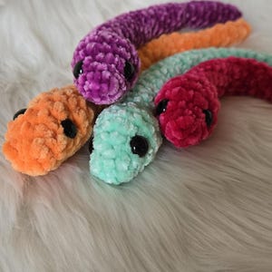 May include: Four plush worm toys in different colors: purple, orange, red, and light green. Each worm has black eyes and a fuzzy texture.
