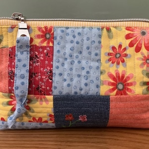 May include: A patchwork fabric zippered pouch with a blue, yellow, red, and pink floral pattern. The pouch has a zipper closure and a fabric loop handle.