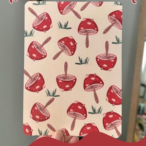 May include: A printable cardstock insert for a Kindle featuring a pattern of red and white mushrooms on a cream background. The text "Pattern B" and "Original Illustration" is printed at the bottom of the insert.