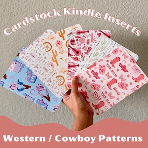 May include: A selection of cardstock Kindle inserts with Western and cowboy patterns is held in a hand. The inserts display designs such as cacti, cowboy boots, guitars, and the text "Howdy". The colour scheme includes pink, blue, and white.