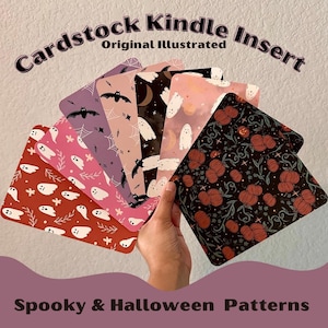 May include: A hand holds a fan of cardstock Kindle inserts with spooky Halloween patterns. The inserts feature bats, ghosts, spiderwebs, and pumpkins in various colors, including red, pink, and black. Text at the top reads "Cardstock Kindle Insert" and "Original Illustrated."