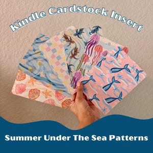 Peut inclure: Une main présente des inserts Kindle en carton avec divers motifs sur le thème marin. Les motifs incluent des coquillages, des étoiles de mer, des méduses et des queues de sirène dans des couleurs pastel. Le texte indique "Kindle Cardstock Insert" et "Summer Under The Sea Patterns".