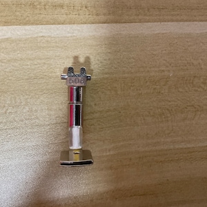May include: A silver sewing machine foot with a number "508" engraved on it.