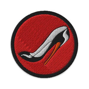 Pode incluir: Um remendo bordado vermelho e preto com um sapato branco de salto alto sobre um fundo vermelho.