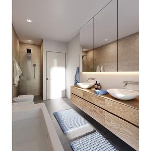 May include: A modern bathroom featuring a floating light wood vanity with two white vessel sinks, a large wall-to-wall mirror with under-cabinet lighting, a white bathtub, a walk-in shower, and two blue textured bath mats on the floor.