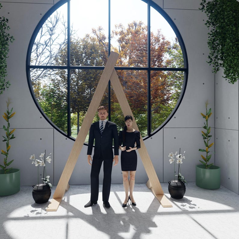 May include: A person in a black suit with a tie and a person in a black dress standing before a large circular window with a light wood A-frame structure. The room features gray paneled walls, potted plants, and white orchid arrangements.