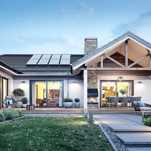 May include: A single-story house with a gabled roof, solar panels, and a stone chimney. The exterior features wood paneling and white walls. A covered patio area includes outdoor furniture, a fireplace, and glass sliding doors.