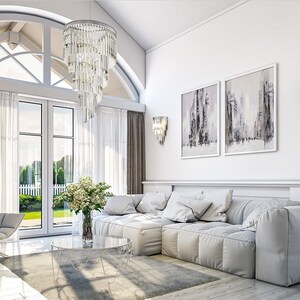 May include: A living room featuring a large white sectional sofa, a gray armchair, a round glass coffee table with a flower vase, a tiered crystal chandelier, two wall sconces, and two framed abstract paintings on a white wall.