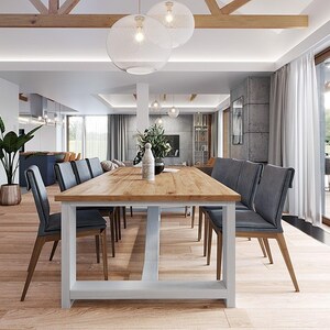 May include: A long rectangular dining table with a light wood grain top and a white base, surrounded by eight dark gray upholstered chairs with wooden legs. The table is positioned in a bright, open-plan room with light wood flooring.