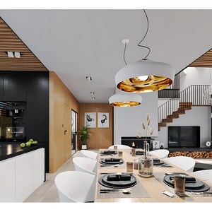 Pu&ograve; includere: Un moderno interno a pianta aperta con una zona pranzo dotata di un lungo tavolo in legno, sedie bianche curve e due grandi lampade a sospensione bianche con interni dorati. La cucina presenta armadietti neri e bianchi.